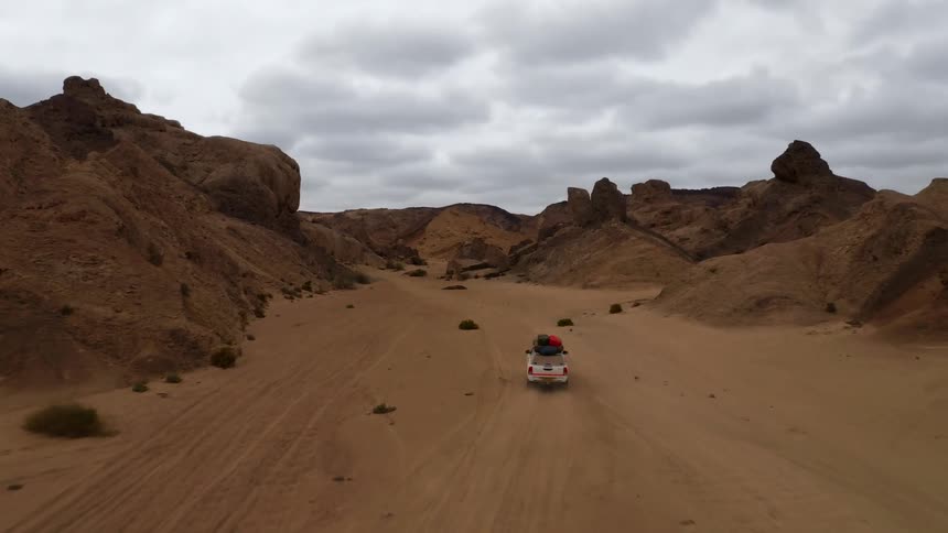 A station wagon with camping equipment drives through the desert