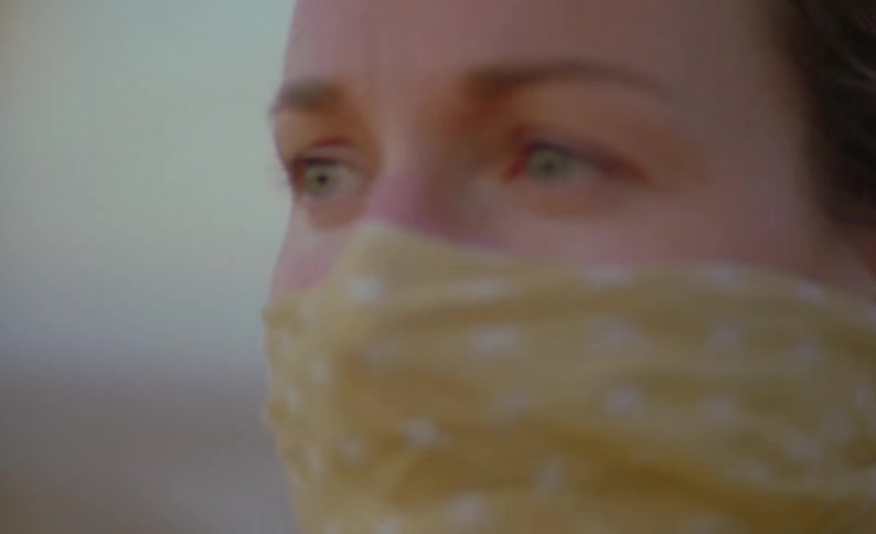 A woman with a yellow bandanna covering her nose and mouth blinks in the wind as she looks around
