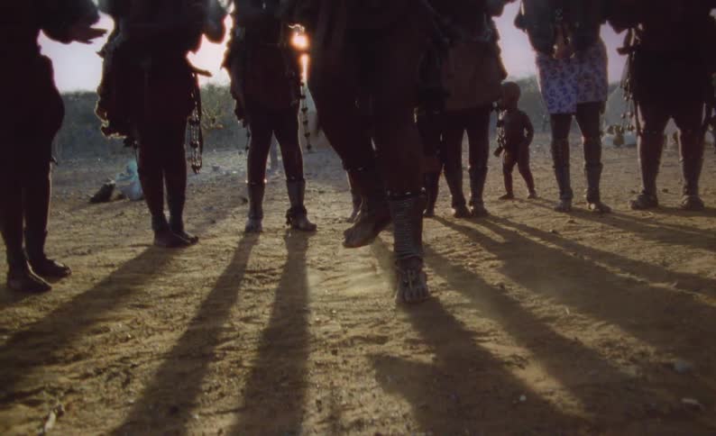 People outside in a rural village a gathered around a man dancing in a forest clearing in the evening