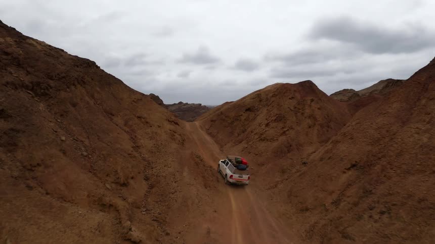A white truck with camping gear on the roof travels up a rugged mountain road