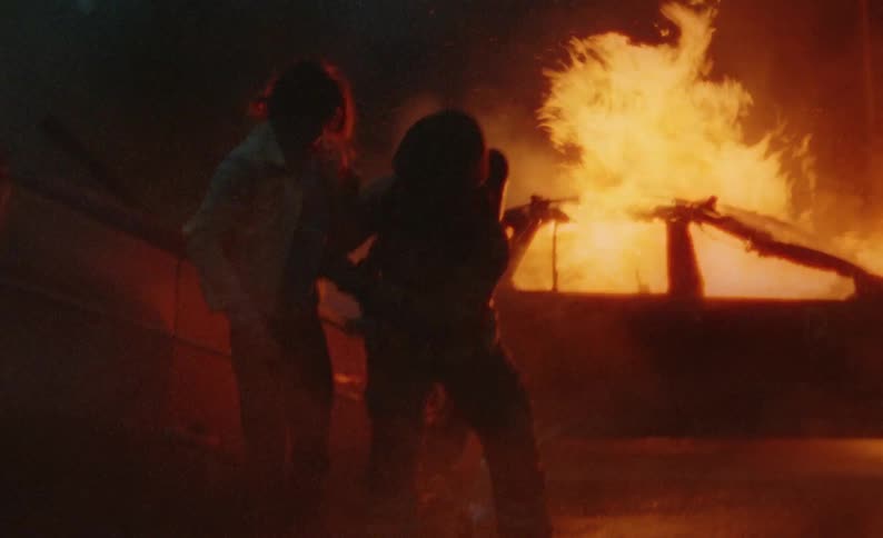 Firefighter helps woman away from wrecked overturned car as other firefighters spray water at burning vehicle