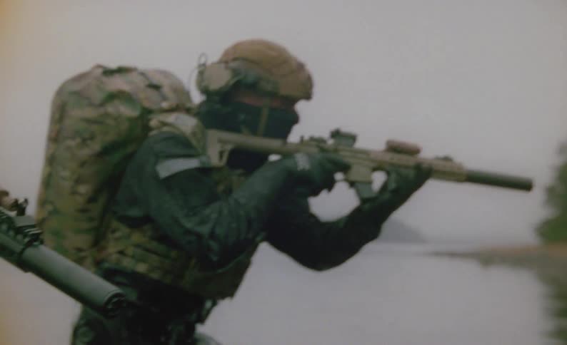 Two men in full military uniforms and gear are walking out of a lake towards the shore on foggy day