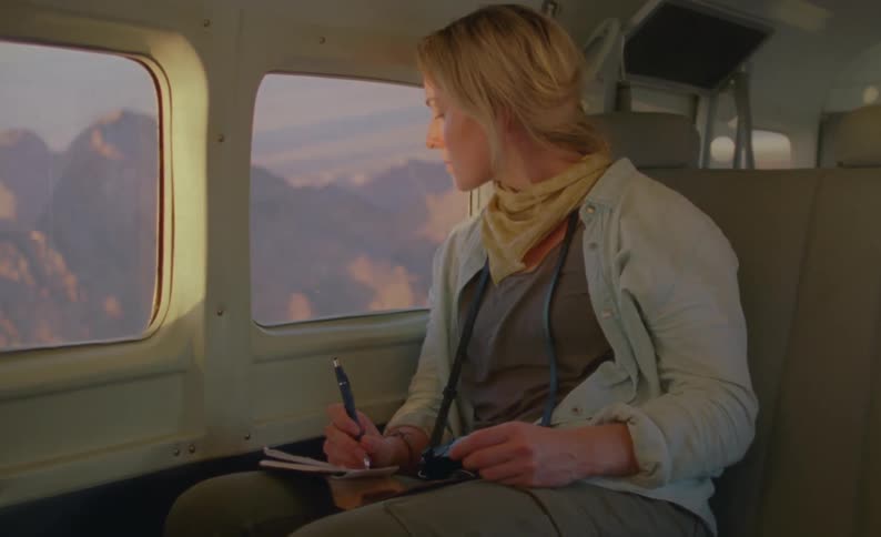 A woman takes notes while sitting in the backseat of a vehicle driving through a canyon