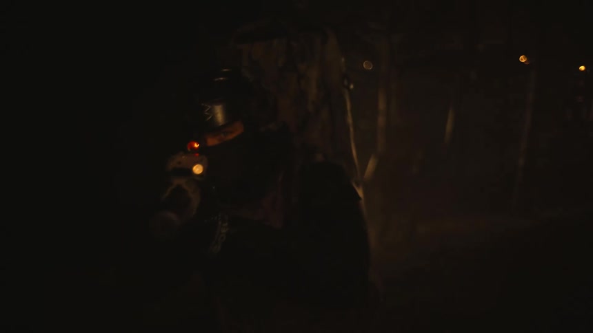 A soldier with his gun raised walks in a forest and then stops and looks side to side
