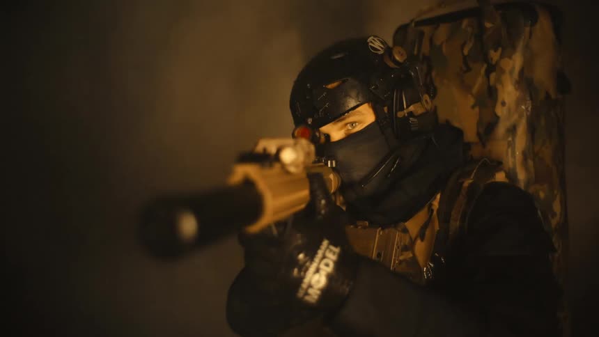 A man dressed in black combat gear with a backpack is kneeling and pointing a rifle at night