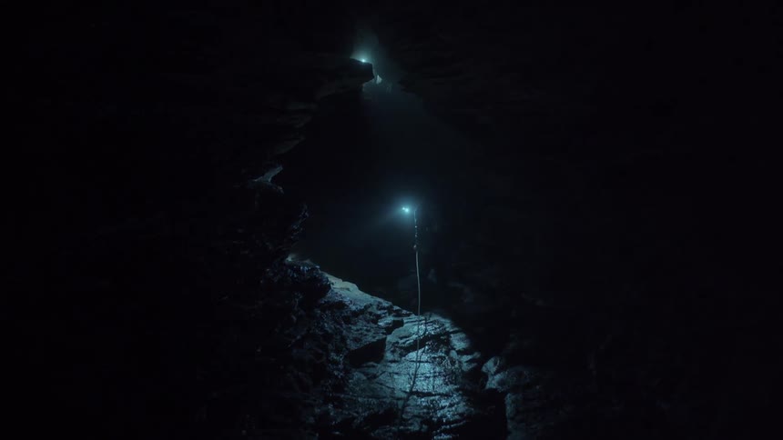 Spelunker tied to a line lights the dark cavern with a headlamp