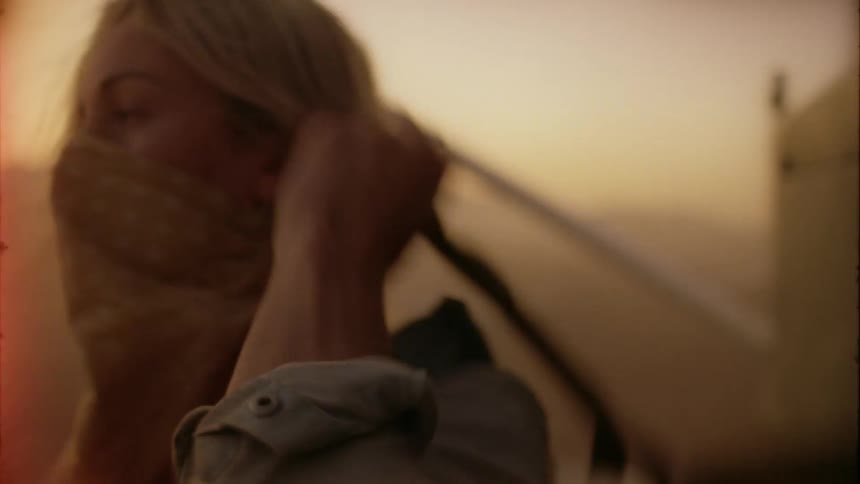 A woman grabs a backpack and covers her face with a scarf for a hike through a windy desert