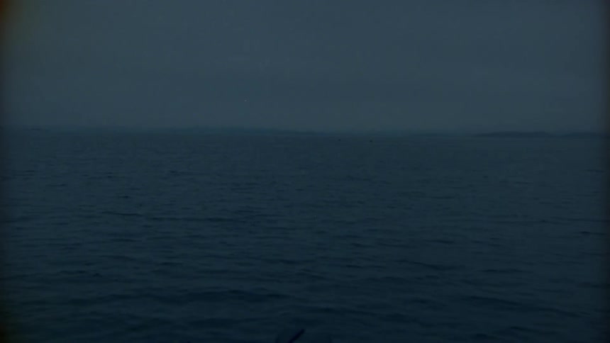 Lighting strikes on hazy horizon near land as waves ripple across ocean surface