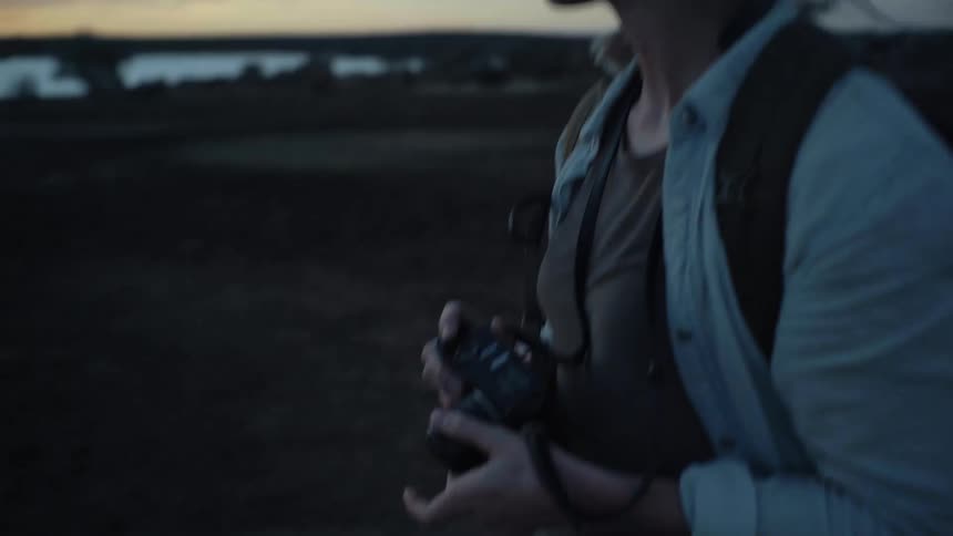 A woman wearing a bandanna is holding a camera outside at dusk