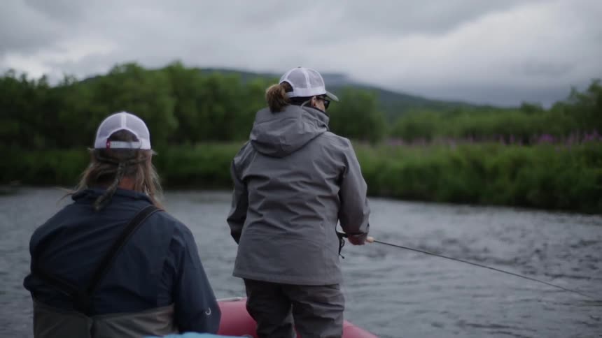 A woman is fishing as a man sits behind her on a raft