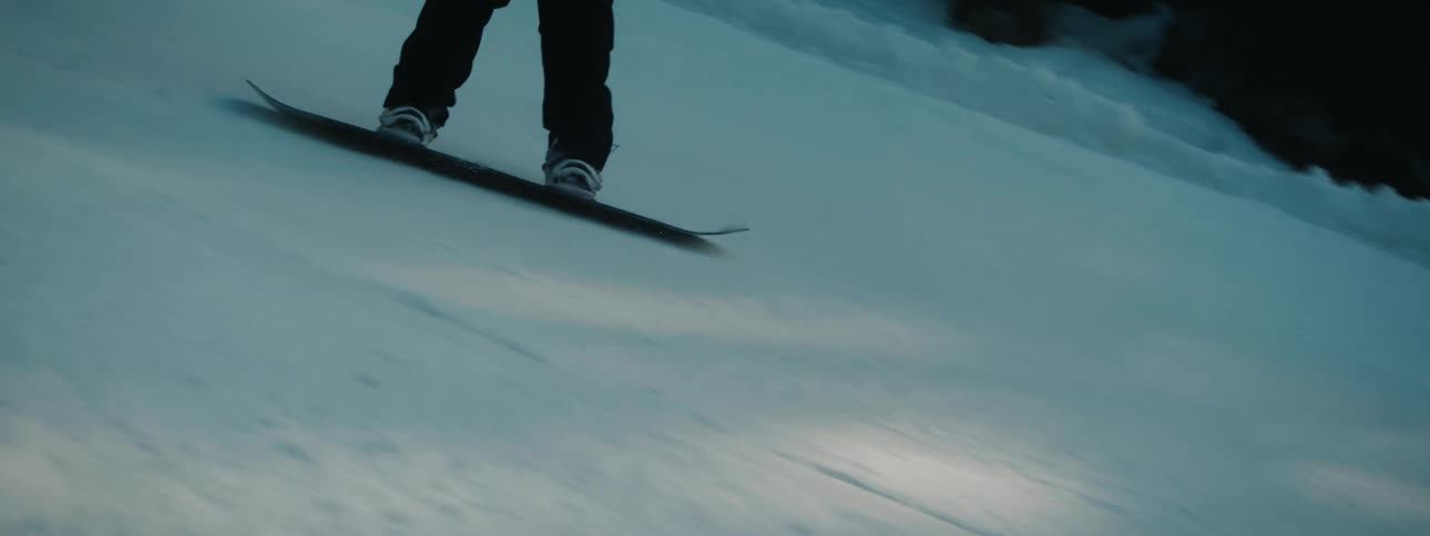 Snowboarder wearing helmet rides board down snowy shady slope