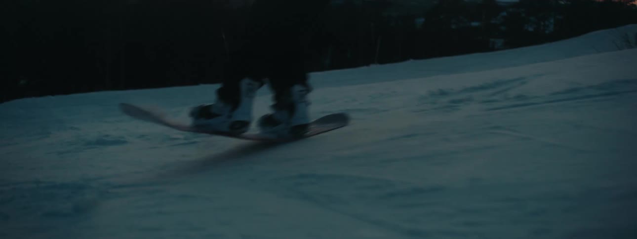 A person snowboarding down a slope with trees the sky and clouds in the background