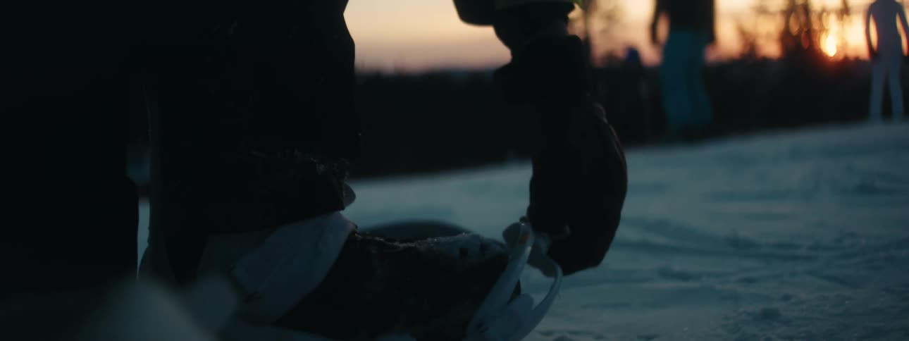 A person putting on a snowboard on snow with trees the sky and clouds in the background