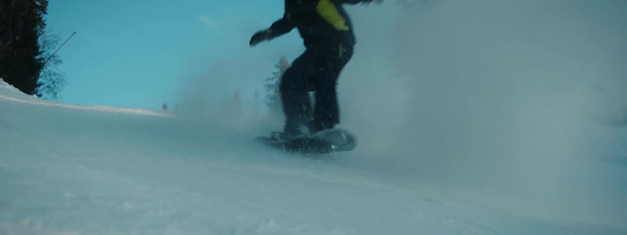 A snowboard rider is going downhill and snow flies in the air as he turns sideways