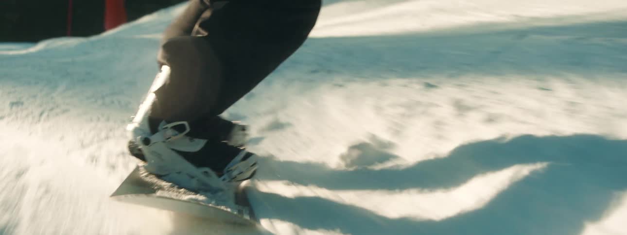 Snowboarder rides down slope passing conifer trees in forest