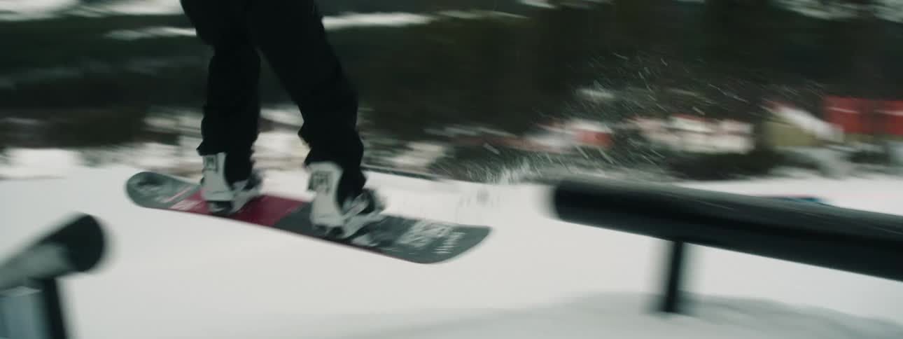 A person snowboarding down a hill jumps on two ramps and then continues snow boarding