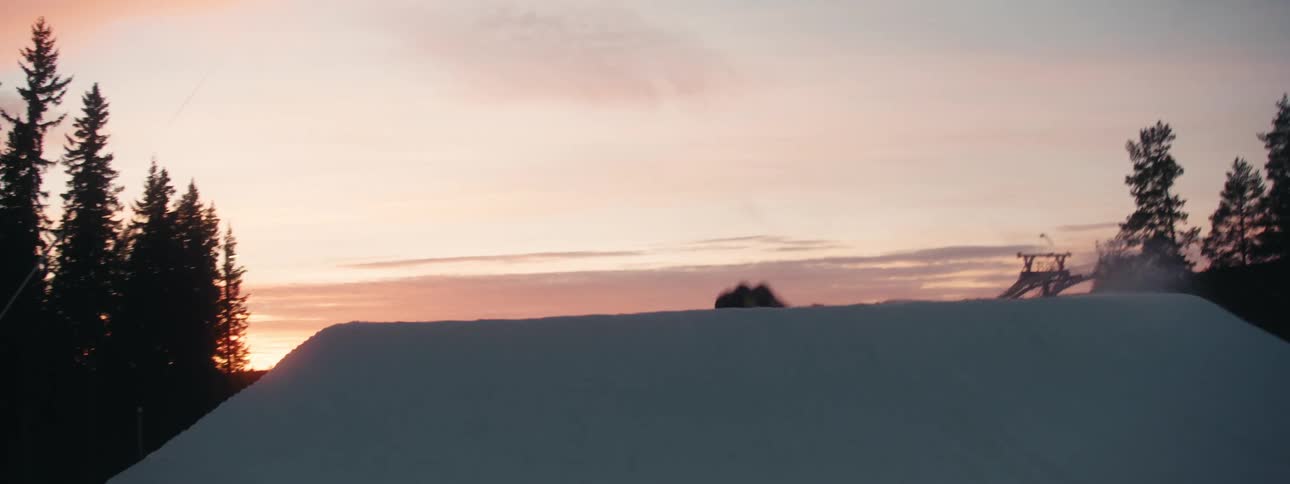 A person snowboarding on a snowy ramp with trees the sky and clouds in the background