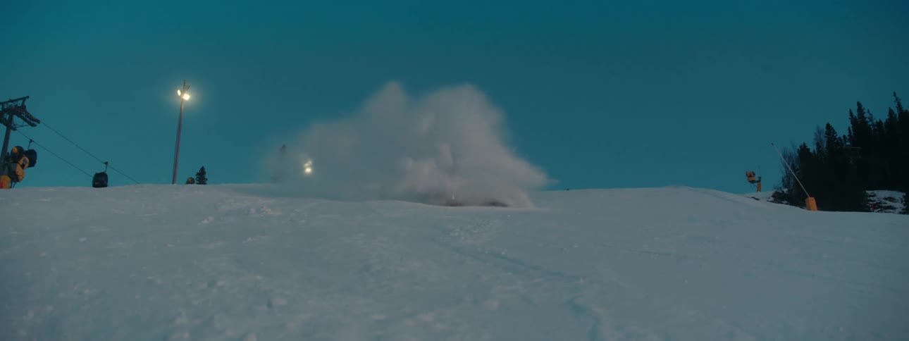 A person snowboarding down a slope with trees the sky and clouds in the background