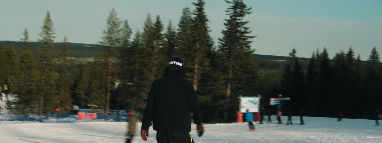A person snowboarding down a slope with trees the sky and clouds in the background