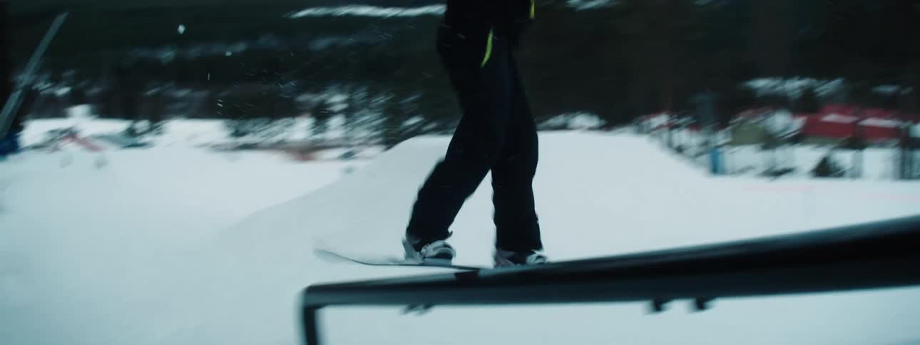 Several people dressed in snow suits are on top of a snow covered hill as one person on a snowboard rides downhill and does a stunt