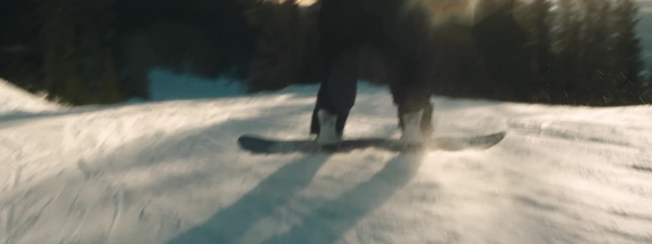 Snowboarder rides snow board down slope taking jump on sunnyday