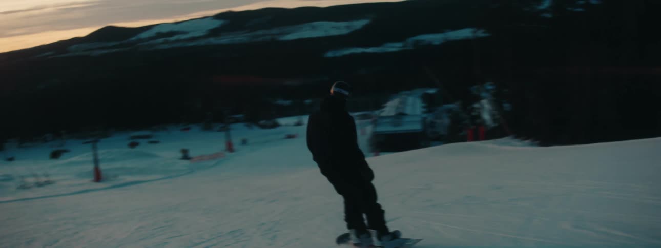 A man rides a snow board down a mountain at dusk