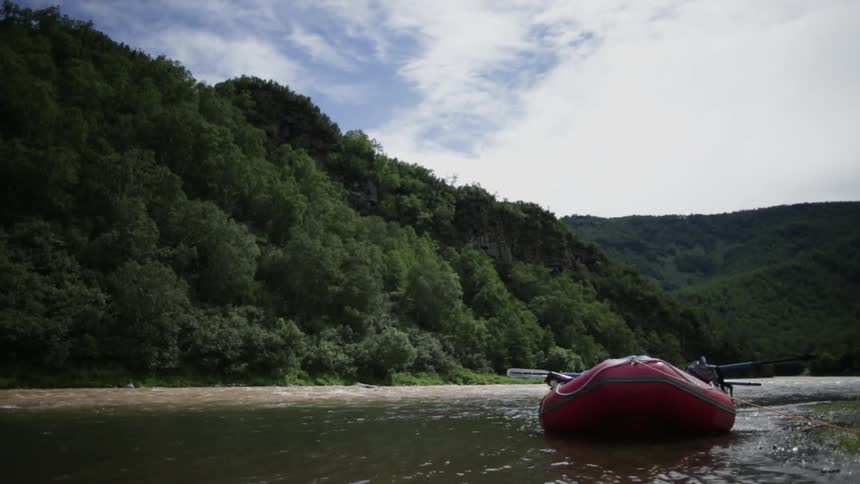 A raft sits docked near the shore as water rushes past