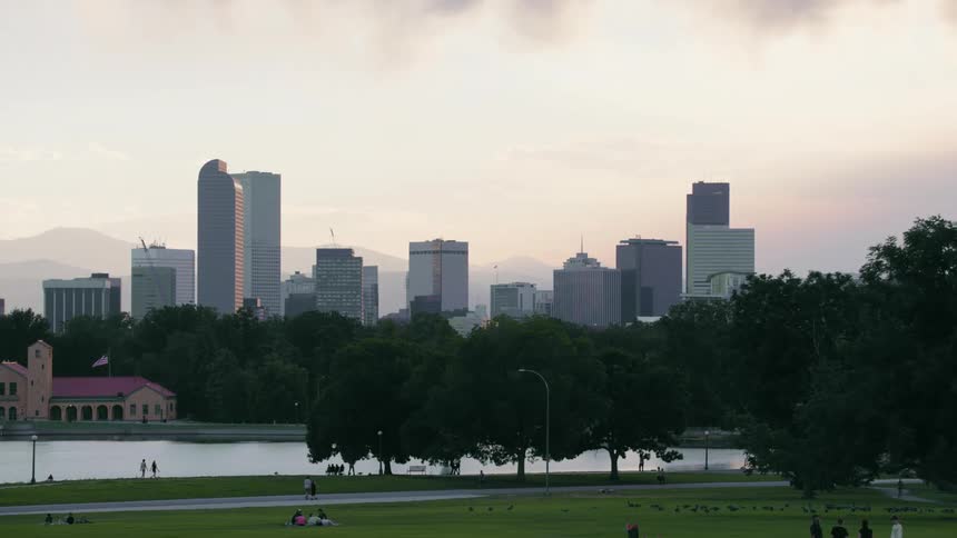 People lounge on the grass and walk on the park path near a city river
