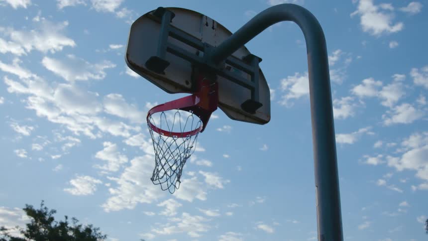 Basketball hoop with intact net stands under cloudy blue sky