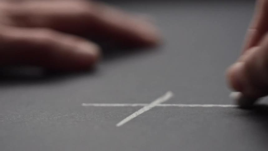 Fingers holding a piece of white chalk draw grid lines on a gray surface