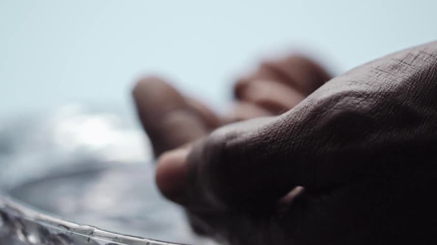 A person washing their hands in a glass bowl with a white background