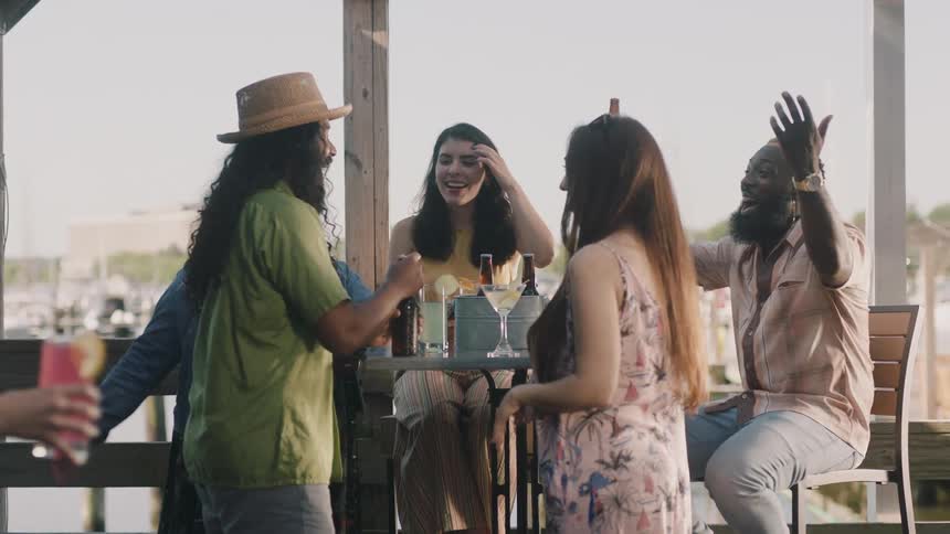 A group of friends is smiling and talking at a table with drinks