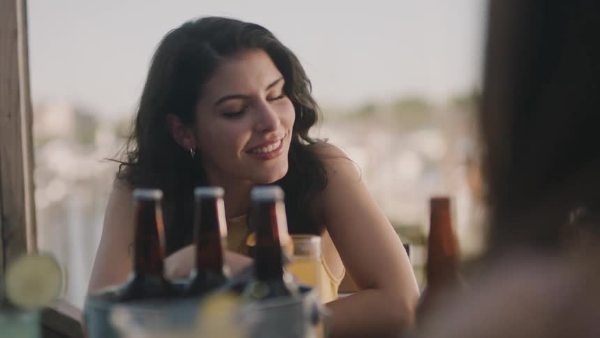 A woman is sitting at a table with drinks and smiling and talking to other people
