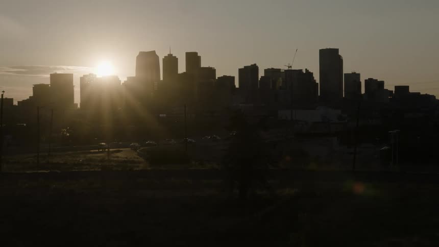 Sun shines past downtown buildings as traffic flows past city skyline