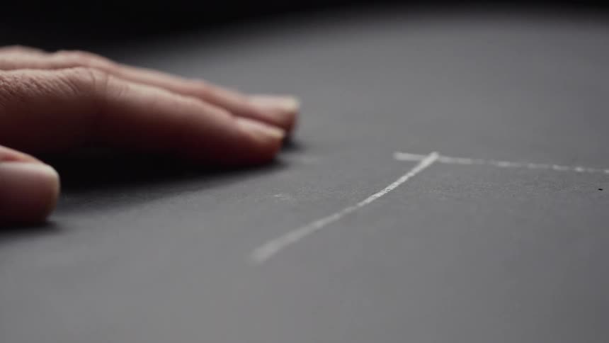 A man draws two perpendicular lines with chalk on black paper