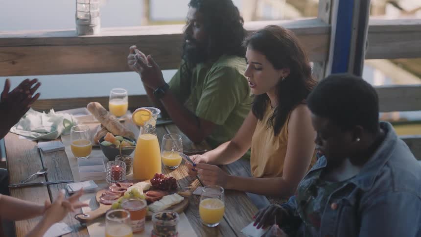 Friends sit at table for brunch talking as water shows through wooden rail