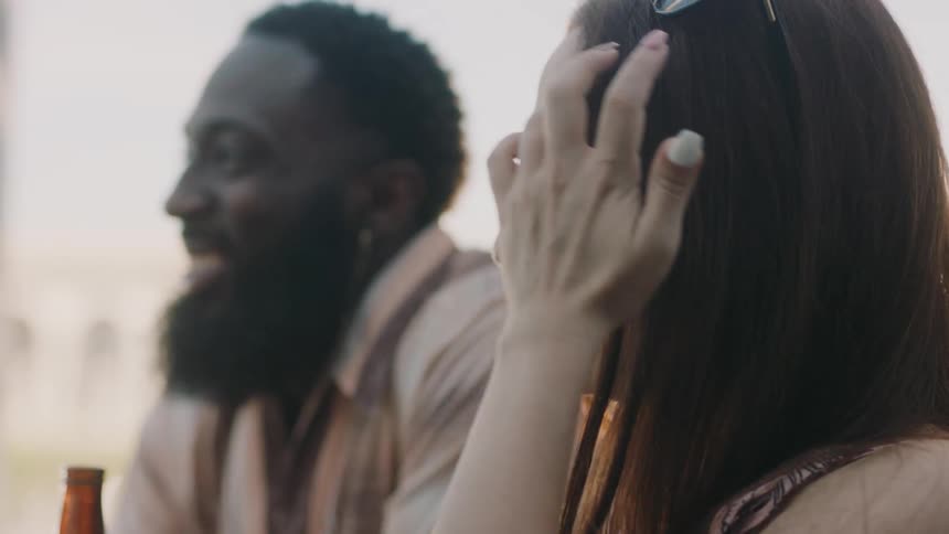Man with beard pink shirt and woman with straight hair sits at table talkto each other