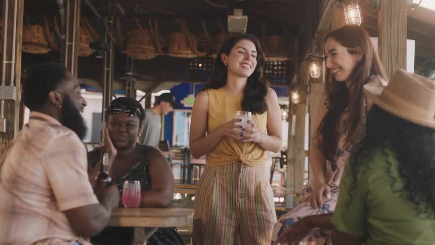 A group of friends standing and sitting in an open air bar laughing and talking