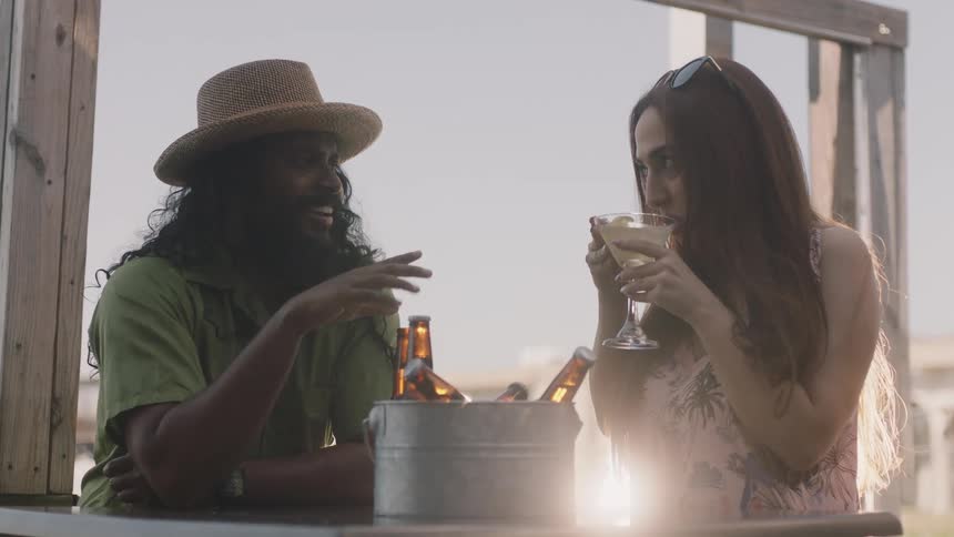 A man and a woman are sitting at a table talking with a bucket of beer bottles on the table