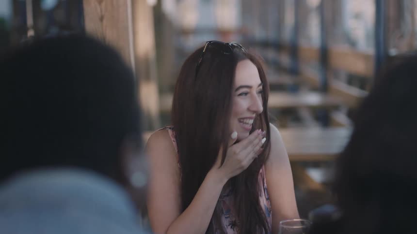 Woman drinking juice stops to cover mouth as she laugh with friends in restaurant