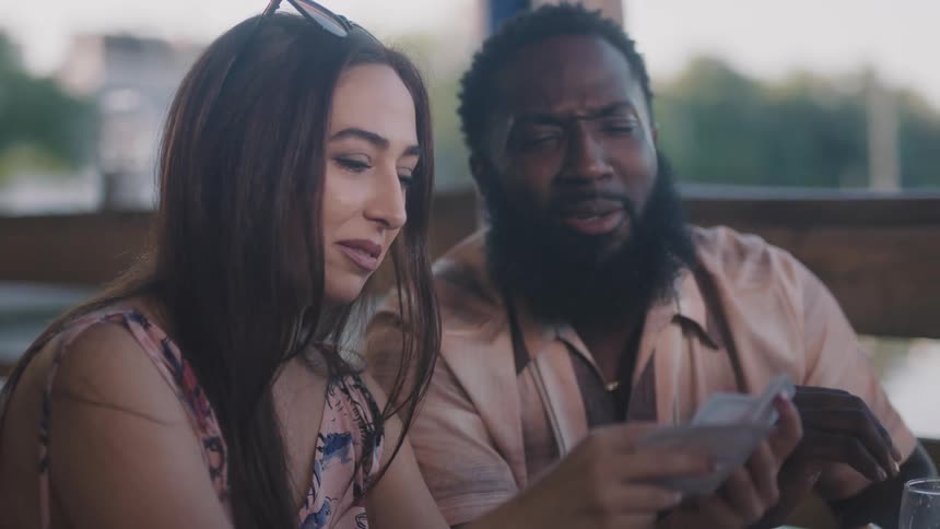 A man and woman flip through playing cards while sitting outdoors