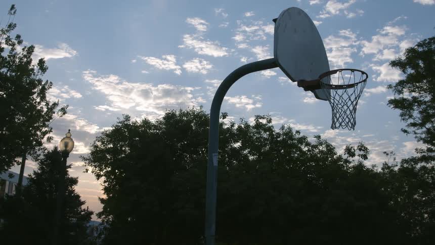 A basketball hoop with trees buildings the sky and clouds in the background