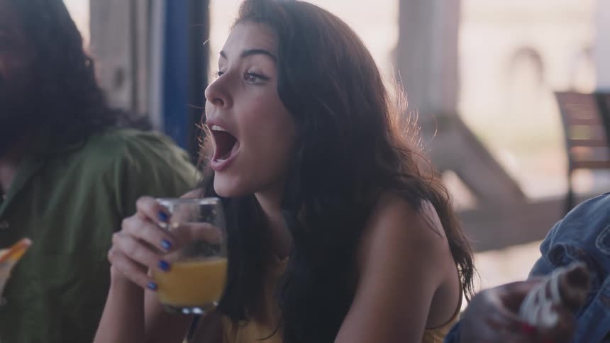 Friends sit at restaurant table talking while holding drink and food