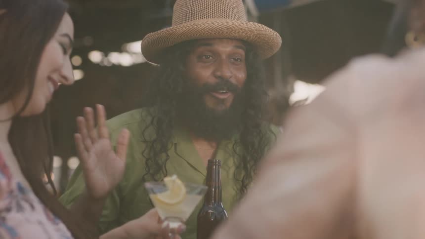 A man with a hat and a bottle in his hand talking to another man with a woman next to them drinking from a glass