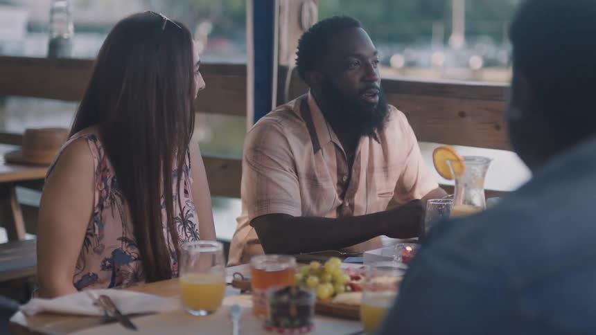 Parents with their daughter and her date have breakfast at a restaurant with outdoor seating near a waterway