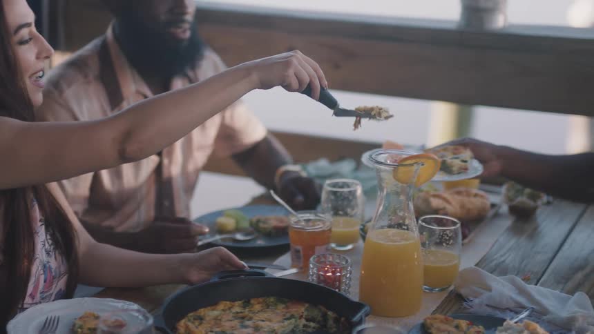 Friends having breakfast at a restaurant where one friend serves another a slice from a giant omelet