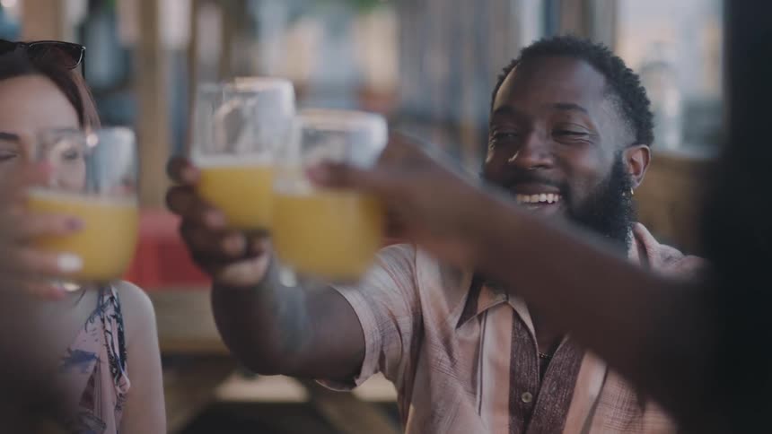 Friends smile and share a toast with orange juice while sitting at restaurant