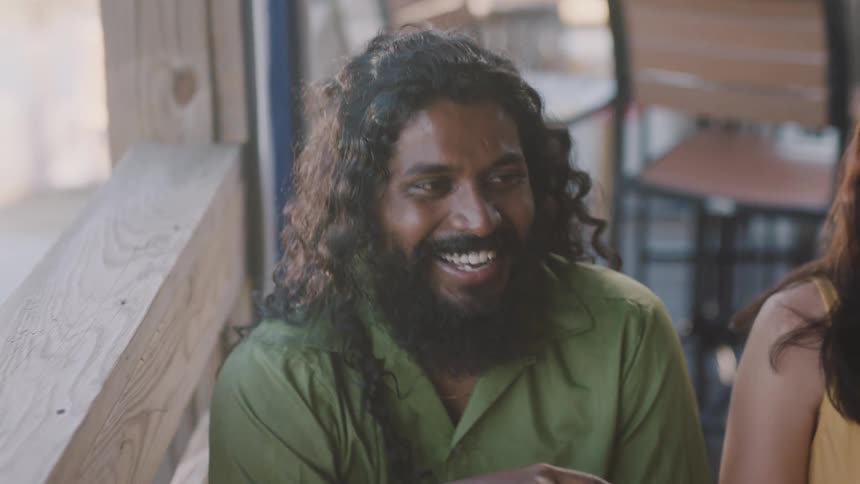 Happy man with long hair and beard laughing and talking with friends in a restaurant