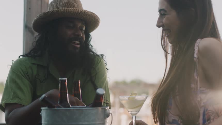A man holding a beer talks with a woman drinking lemonade at an outdoor table during the day