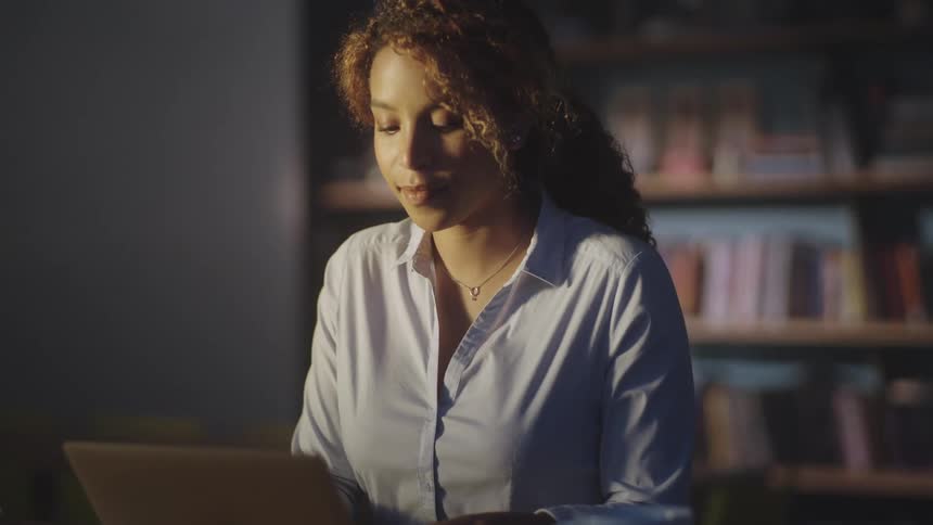 A woman sits at her desk and writes on a tablet with her stylus and then types on her laptop as she concentrates